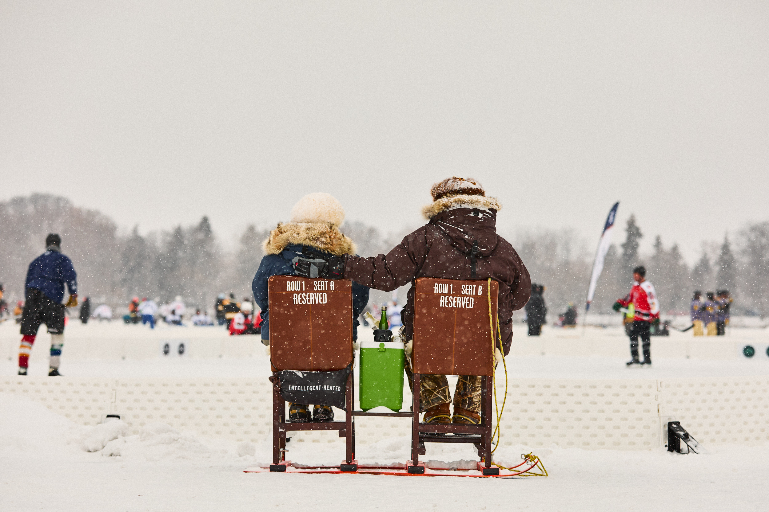 Couple Sits on homemade chairs to watch Pond Hockey